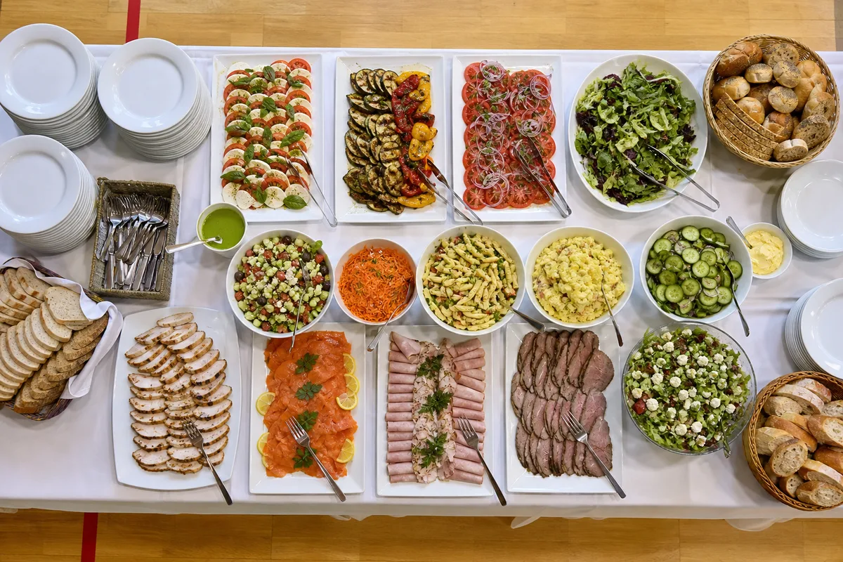 Buffet froid dressé sur une table associative, plats et assiettes prêts à être servis